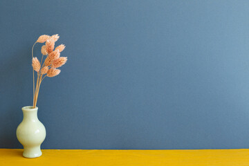 Vase of pink dry flowers on yellow wooden table. blue wall background. home interior