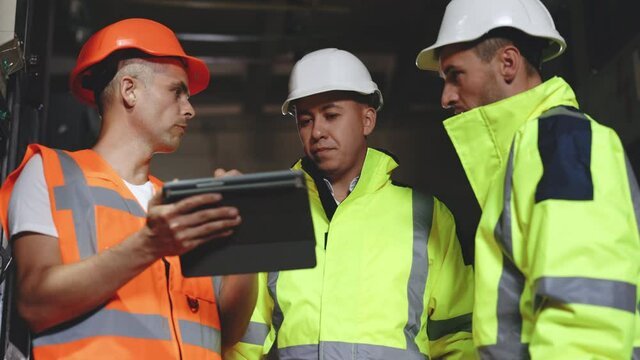 Three Heavy Industry Engineers and Worker Stand in Pipe Manufacturing Factory, Use Digital Tablet Computer, Have Discussion. Design and Construction of Oil, Gas and Fuels Transport Pipeline