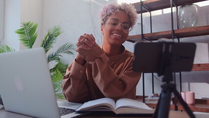 Young friendly African American woman is recording her video blog. Woman sitting in her home office...