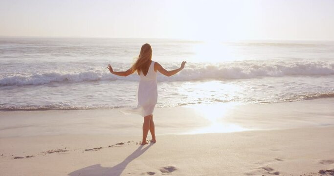 Free happy woman enjoying sunset. beautiful woman in white dress embracing the golden sunshine glow of sunset with arms outspread and face raised in sky enjoying peace, serenity in nature