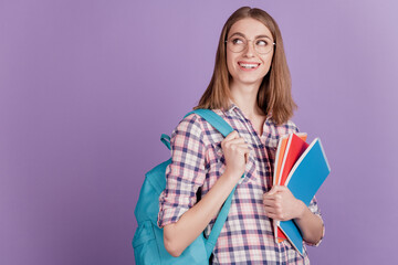 Portrait of sweet young girl student holding notebook in her hands bag study think dream isolated on violet color background