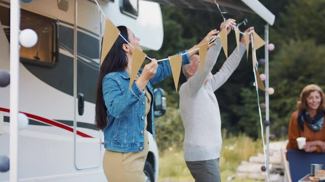 Multi-generation family preparing party by car outdoors in campsite, caravan holiday trip.
