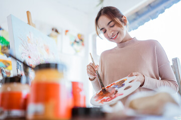 asian female painter painting on canvas in her workshop