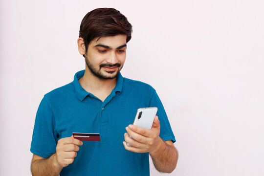Handsome man makes a payment, using a credit card and smartphone. Photo of indian man in t-shirt on isolated background.