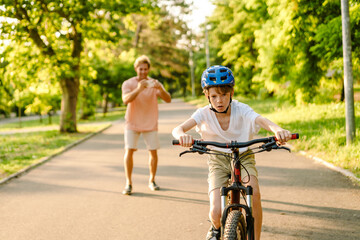 Ginger white man taking photo on cellphone while his son riding bicycle