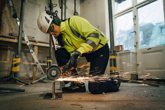 Full length of female construction worker cutting metal while using electric saw at site