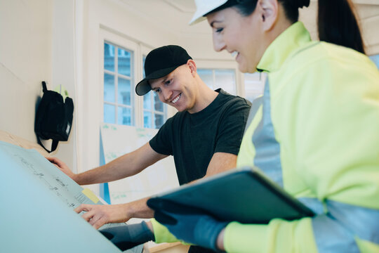 Happy male worker and female building contractor discussing over blueprint in office