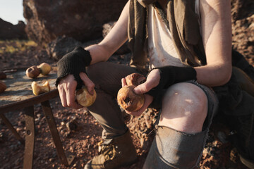 Close-up of homeless woman in torn clothes holding spoiled fruits while sitting on the rock