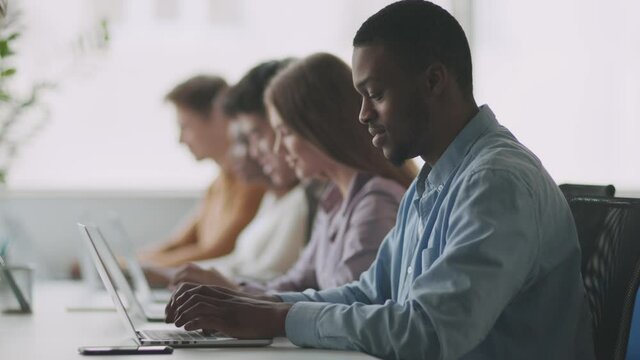 Modern technologies and education. Young african american guy student typing on laptop, sitting with group of groupmates