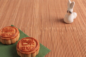 Chinese moon cake and the rabbit is a symbol of autumn on a bamboo mat background. Asian traditional mid-autumn festival. Translation of hieroglyphs: mango, pomegranate and lotus