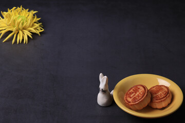 Fototapeta na wymiar Chinese moon cake and the chrysanthemum is a symbol of autumn on a dark gray background. Asian traditional mid-autumn festival. Translation of hieroglyphs: mango, pomegranate and lotus.