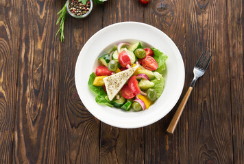 Fresh Greek salad with feta cheese, tomatoes, cucumber, pepper, olives, red onion and lettuce on wooden table, top view. Healthy food, vegetarian dieting, cooking at home concept