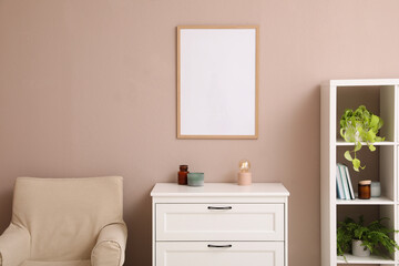 Empty frame hanging on pale rose wall over chest of drawers in living room. Mockup for design
