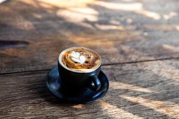 Black cup of cappuccino with latte art on saucer on wooden background
