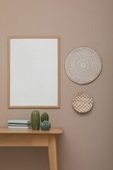 Empty frame hanging on beige wall over wooden table with decor. Mockup for design