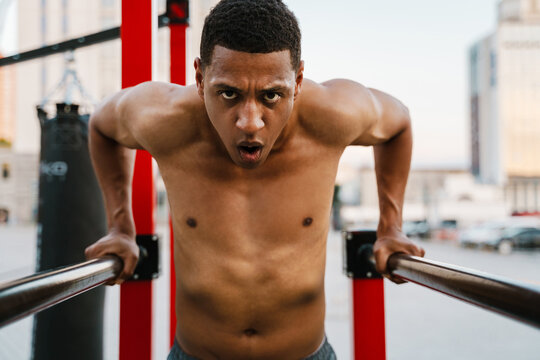 Black shirtless sportsman doing exercise on parallel bars working out
