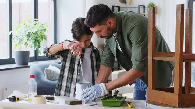 repair, diy and home improvement concept - father and son in protective gloves stirring grey color paint in can for painting old wooden table at home
