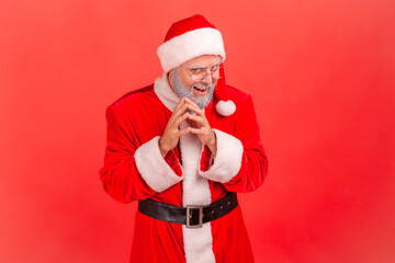 Insidious elderly man with gray beard wearing santa claus costume looking at camera with cunning...