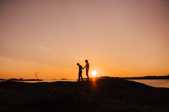 Male friends holding hands while walking at lakeshore during sunset