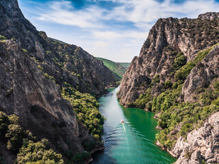 Drone view of Matka Canyon. Drone shot of a lake in a canyon in North Macedonia. Rocky green slopes. Transparent water surface of the lake. Mountain trail along the river. Lake in the mountains - obrazy, fototapety, plakaty