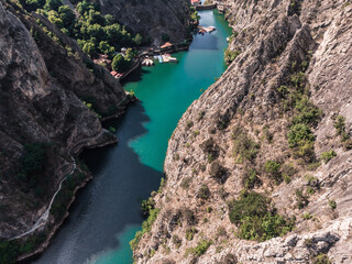 Fototapeta na wymiar Drone view of Matka Canyon. Drone shot of a lake in a canyon in North Macedonia. Rocky green slopes. Transparent water surface of the lake. Mountain trail along the river. Lake in the mountains