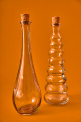 Empty glass bottle with original shapes on a solid neutral colored background.