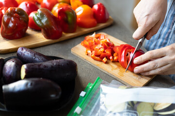 A woman cuts red peppers and eggplants into pieces and puts them in plastic freezer bags. Freezing vegetable.