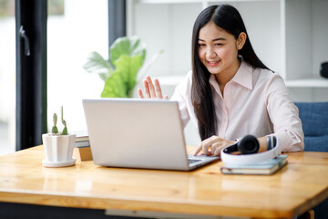 Young asian woman having conference video call using laptop talking to coworker online audience sitting at office desk in evening.	
