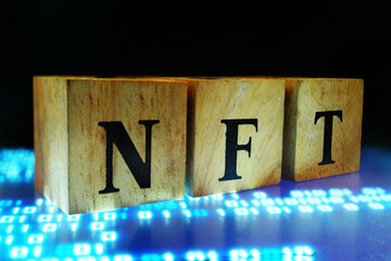 Text NFT on wood cube block decorate on blue digital background for NFT art market concept.   