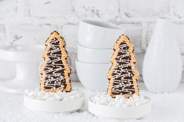 Two cookies shaped as christmas trees with chocolate and sugar glaze in bowls with coarse sugar on...