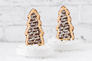 Two cookies shaped as christmas trees with chocolate and sugar glaze in bowls with coarse sugar on white background