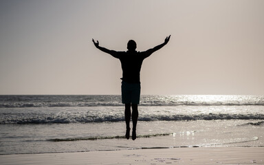 silhouette of athletic man jumping with raised hands on summer beach, freedom