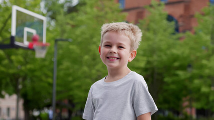 Portrait of cute blonde preschooler boy at basketball playground looking at camera