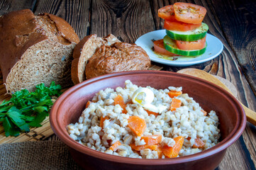 Delicious healthy food. Vegetarian crumbly pearl barley porridge with carrots in a clay bowl.
