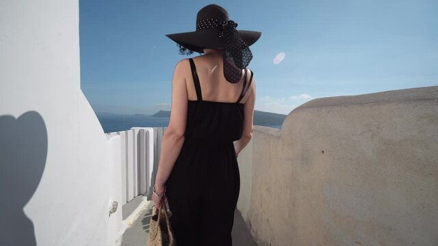 Elegant brunette woman in Oia on Santorini walking on narrow street and open old wooden door with private space sign