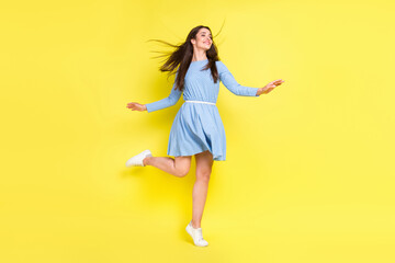 Photo of cute pretty young woman dressed blue clothes dancing looking empty space smiling isolated yellow color background