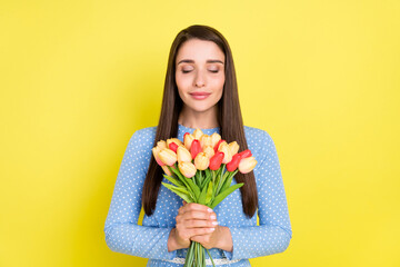 Photo of dreamy inspired peaceful girl hold tulips close eyes wear dotted blue dress isolated yellow color background