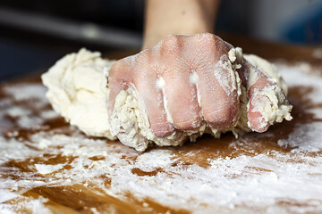 female hand kneading a flour dough by rolling it on a wooden board