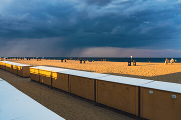 Beach ocean view with beach lockers in foreground, at sunset. Rainstorm in distance over water. 