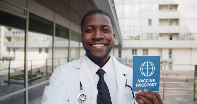 African doctor looking at camera and talking holding vaccine passport