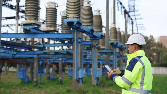 Electrical worker engineer working with digital tablet near tower with electricity. Energy business technology industry concept. Electrical engineer studying reading on tablet