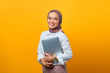 Portrait of smiling Asian woman bring laptop over yellow background