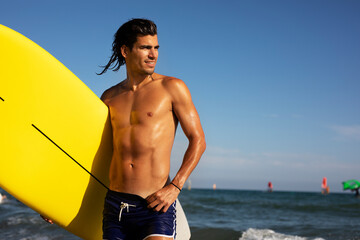 Portrait of handsome surfer with his surfboard. Young man with a surfboard on the beach