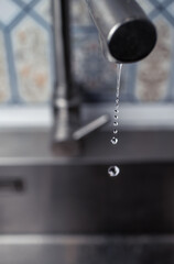 Drops of water from the mixer drip into the kitchen sink. Selective focus.