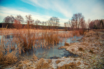 View of the countryside and frozen winding brook in the evening at sunset light
