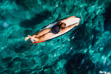 Fototapeta na wymiar Surf girl on surfboard in transparent turquoise ocean. Aerial view with surfer woman