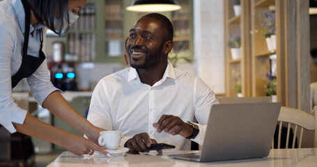 Waitress in safety mask serve coffee for businessman in restaurant