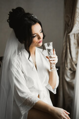Beautiful and lovely bride in night gown and veil sitting and drinking champagne