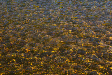 The texture of the water surface in a clear river, the stone bottom shines through on a bright sunny day