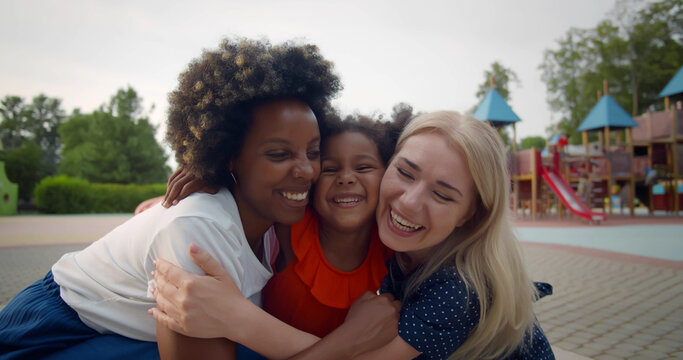 Multiethnic Lesbian Couple And Adopted Little Daughter Hugging On Playground